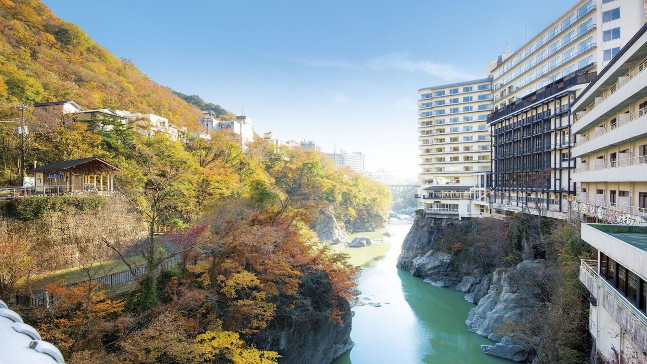 Hotel Sunshine Kinugawa perched above the jade-green Kinugawa river, autumn maples turning on the opposite bank.